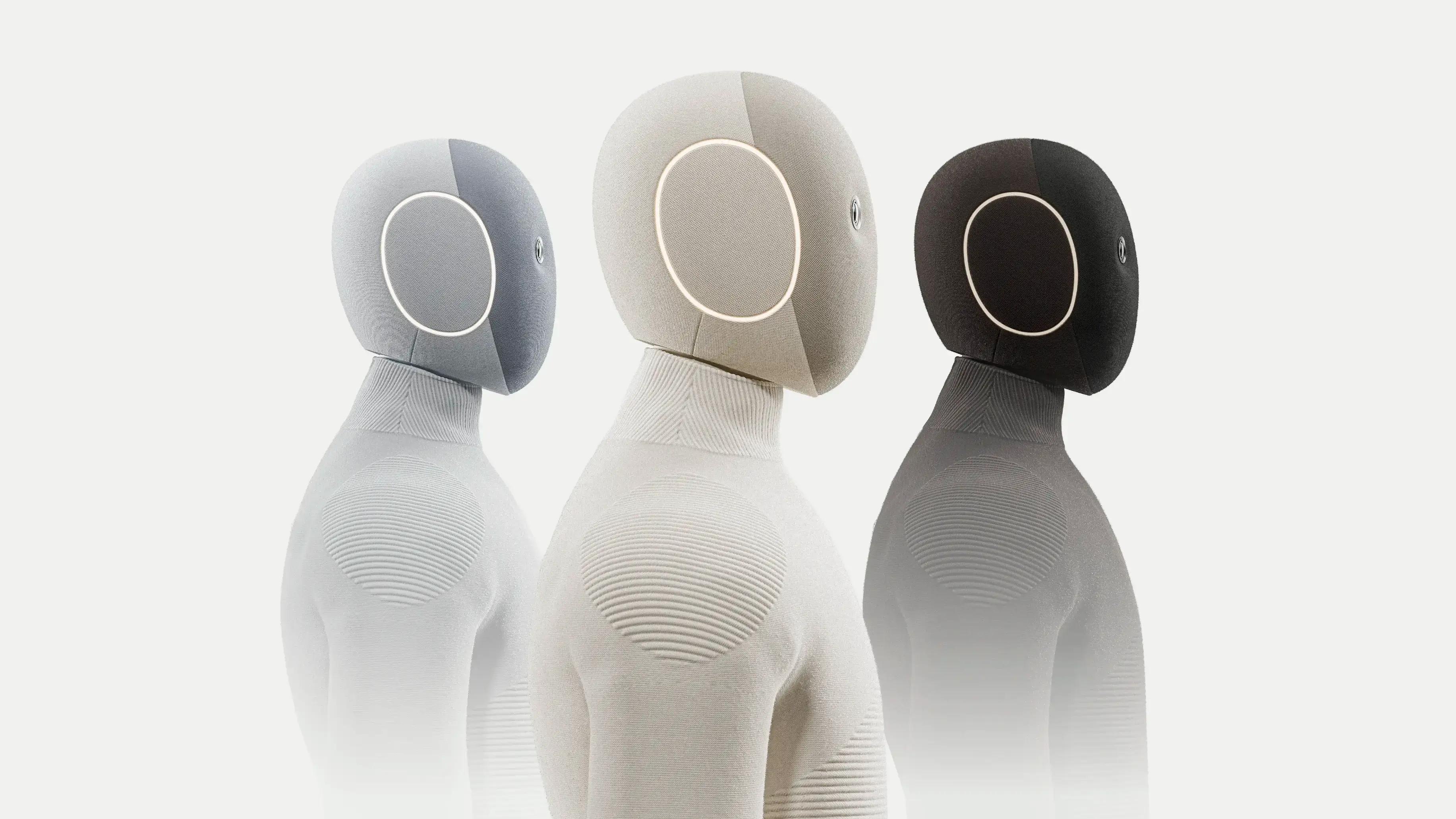 Tres unidades de NEO en distintos colores: robot humanoide doméstico de 1X con traje blando y anillos luminosos en la cabeza