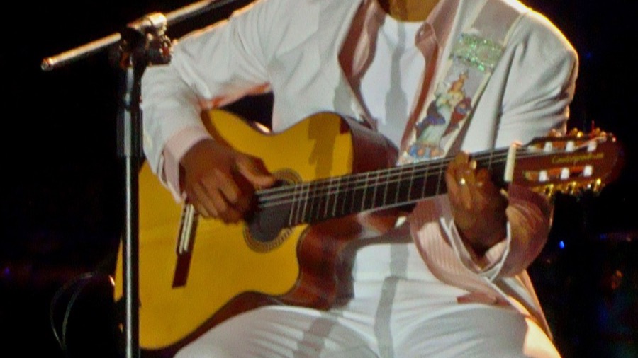 Alexandre Pires cantando en su proyecto Em Casa ao Vivo, con micrófono en mano y fondo de estudio