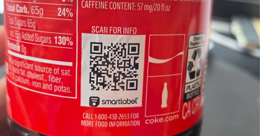 Primer plano del QR SmartLabel en una botella de Coca-Cola con «SCAN FOR INFO», logo smartlabel, 65 g de azúcares añadidos y 57 mg de cafeína por 20 fl oz