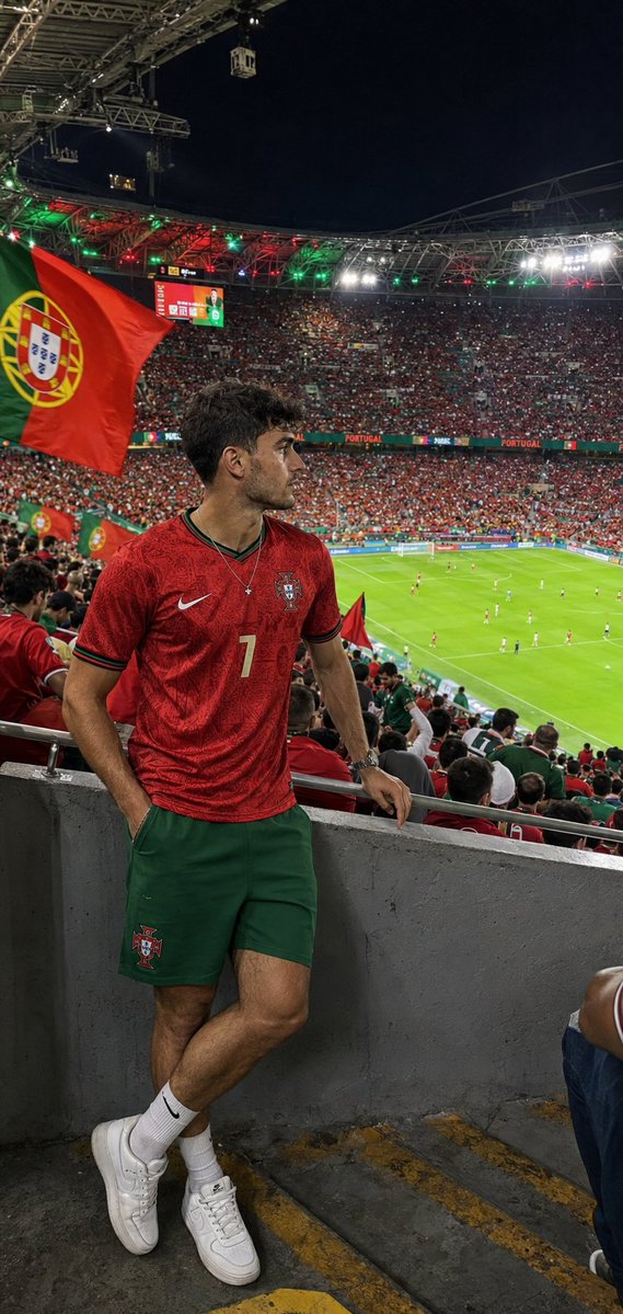 Foto generada con GPT Image 2: aficionado de Portugal en grada alta del estadio con camiseta roja y partido visible al fondo